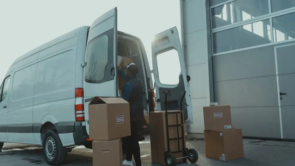 A mover loading labelled boxes into a van using a hand trolley